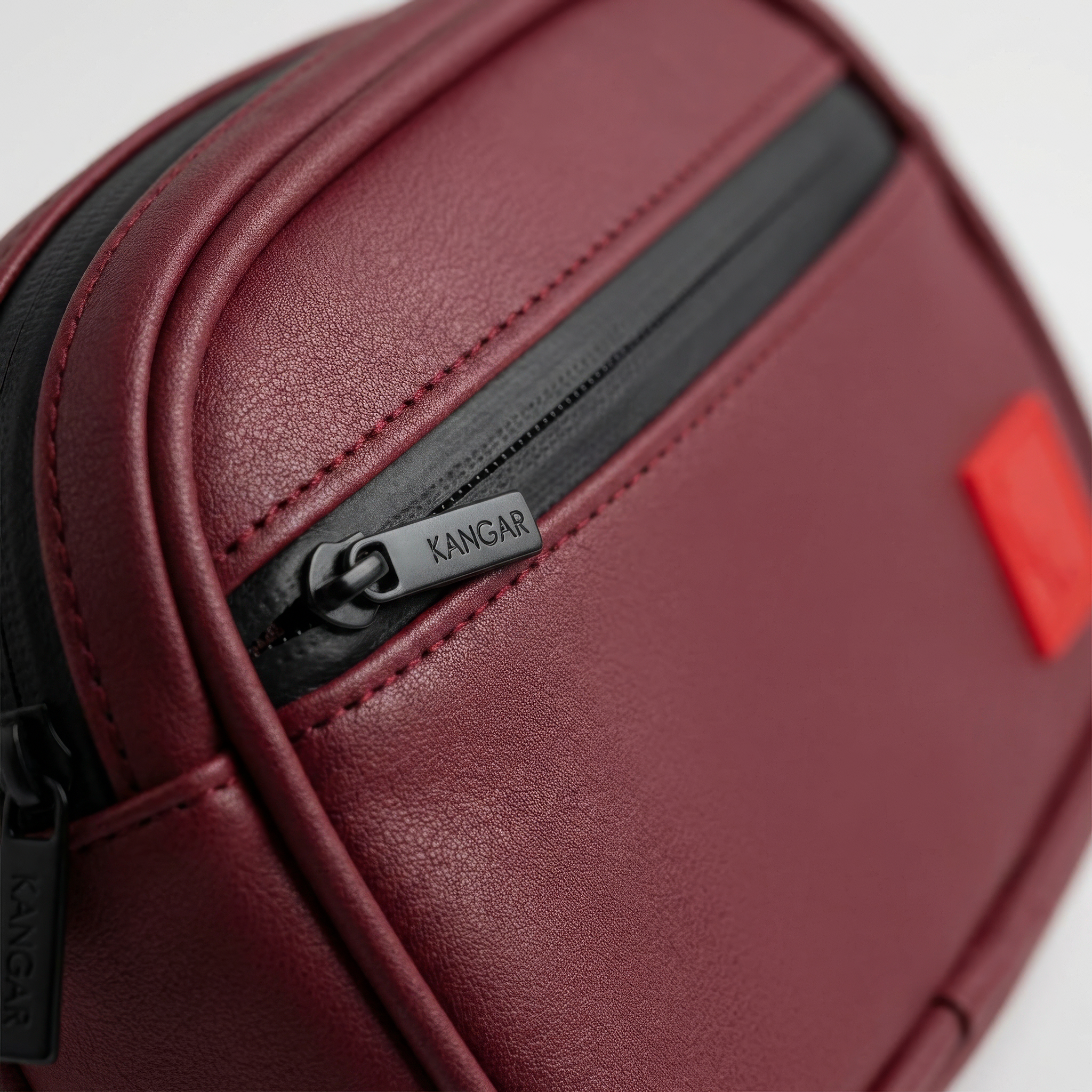 Maroon leather case with black zipper and red tag on a white background Detachable utility pouch with waterproof zipper and logo patch