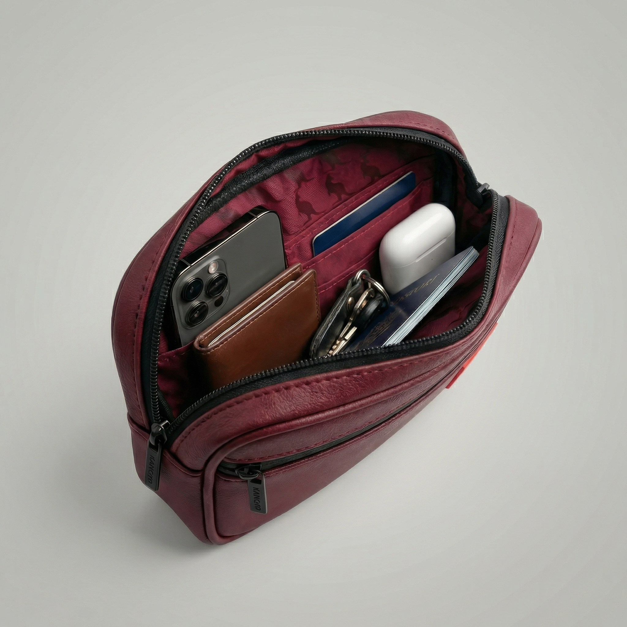 Open maroon leather pouch with phone, wallet, and keys Detachable utility pouch with waterproof zipper and logo patch