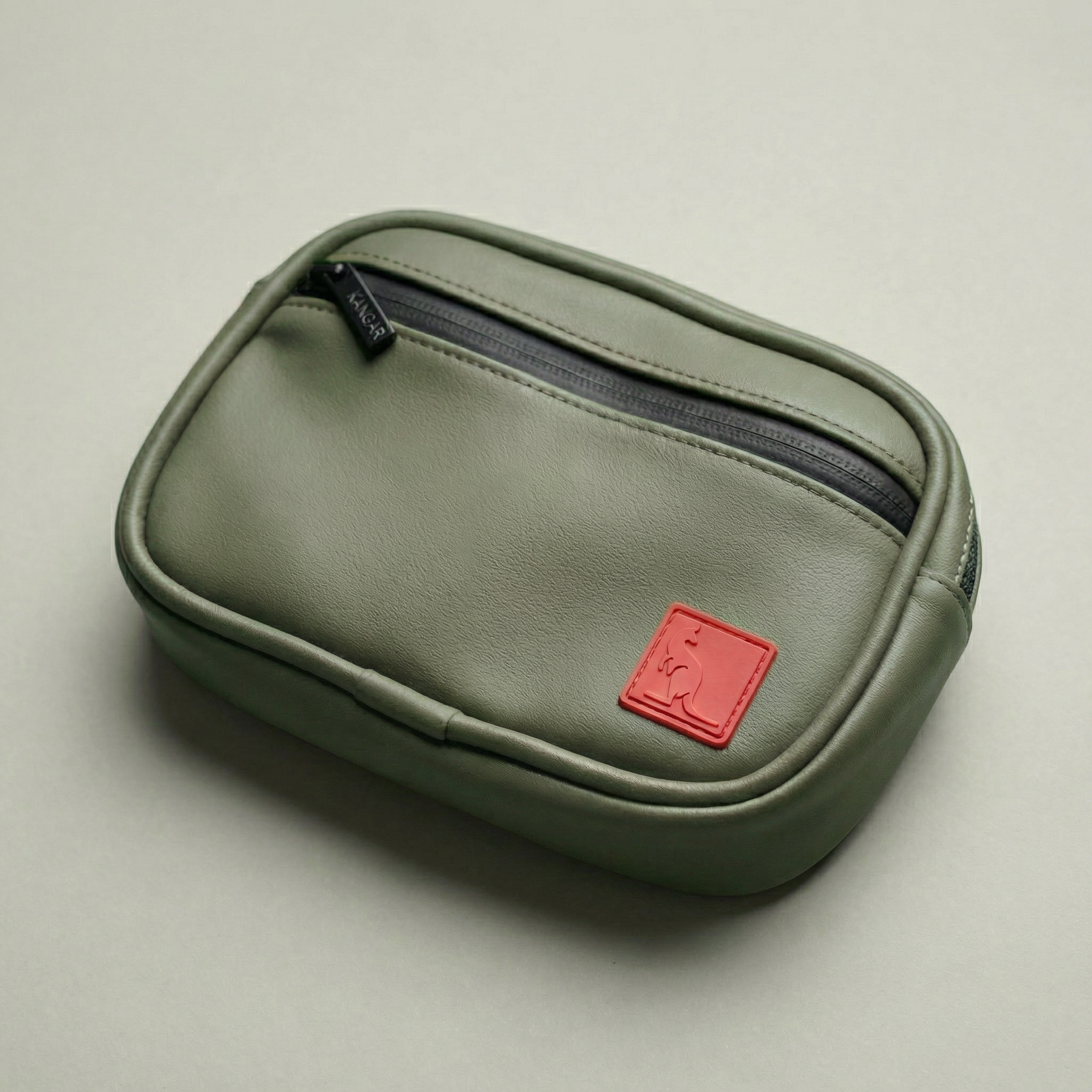 Green pouch with a red label on a beige background Detachable utility pouch with waterproof zipper and logo patch