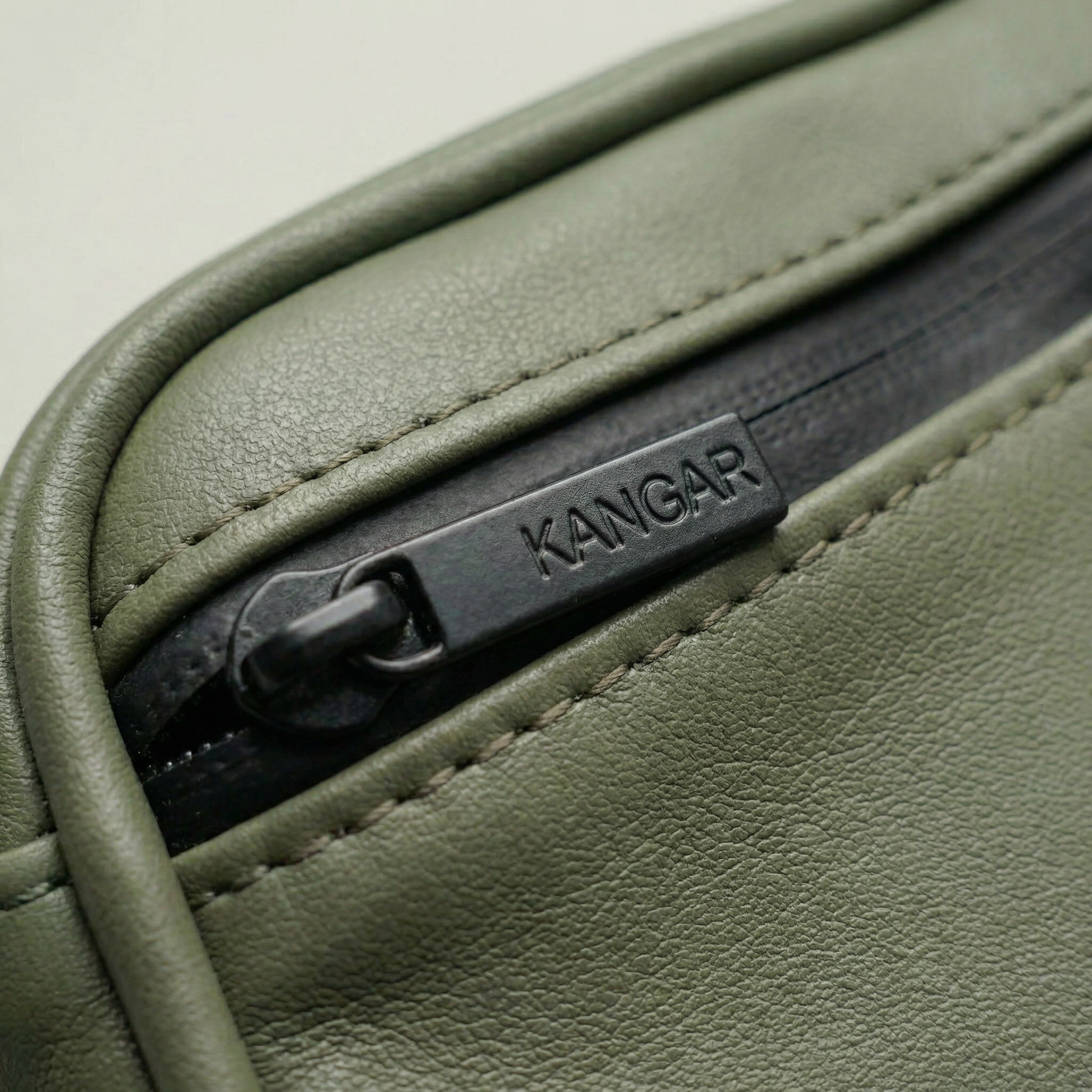 Close-up of a green leather product with a Kangar label on a beige  Detachable utility pouch with waterproof zipper and logo patchbackground