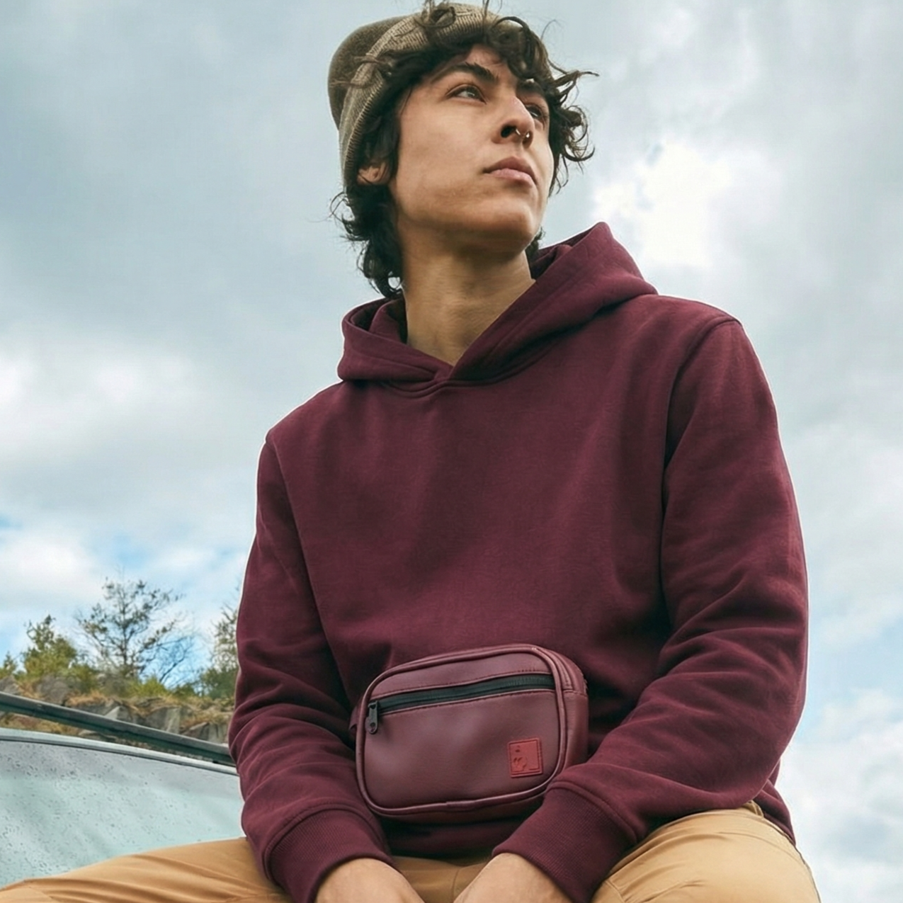 Person wearing a maroon hoodie and carrying a matching fanny pack  KANGAR Hoodie System in Oxblood with detachable utility pouchoutdoors.